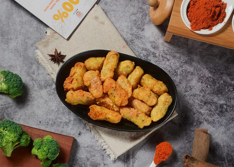 Golden fried snacks on a black platter surrounded by fresh spices and vegetables.