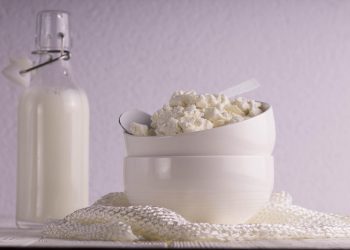 Cottage cheese in a bowl with a milk bottle in the background.
