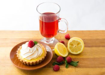 Lemon tart with raspberry and red tea on wooden table.