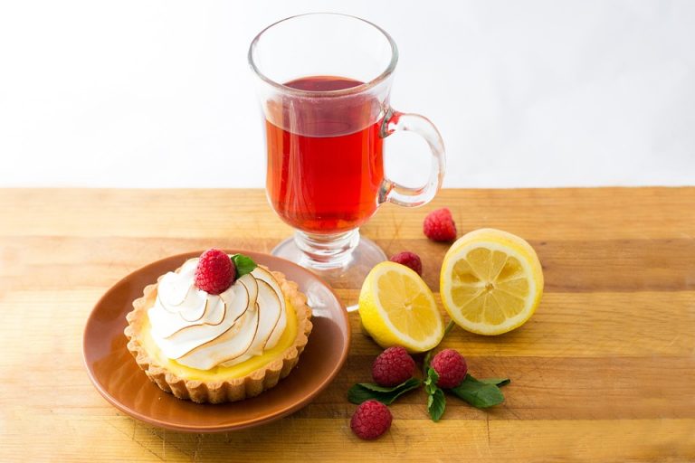 Lemon tart with raspberry and red tea on wooden table.