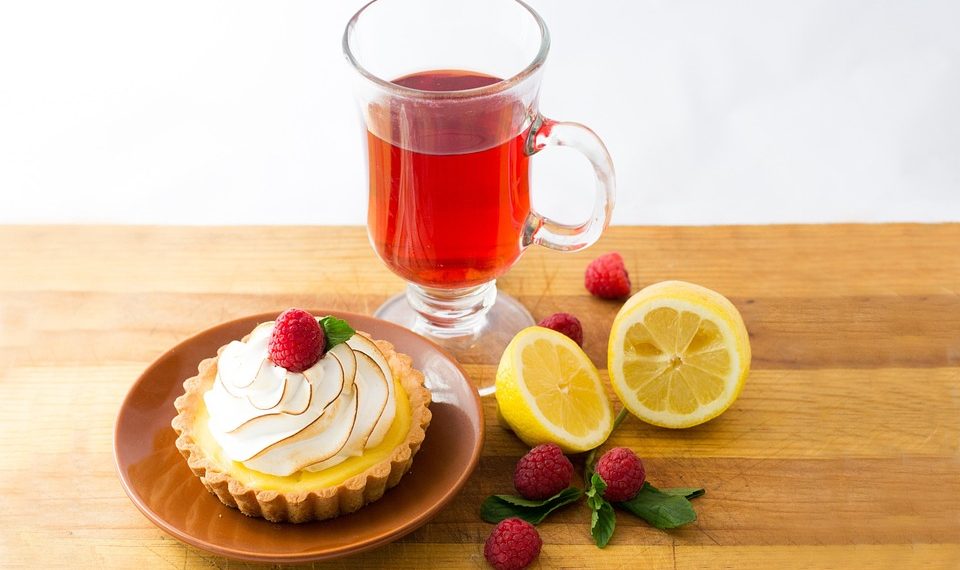 Lemon tart with raspberry and red tea on wooden table.