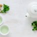 White teapot and cups with mint leaves and sugar cubes on a table.