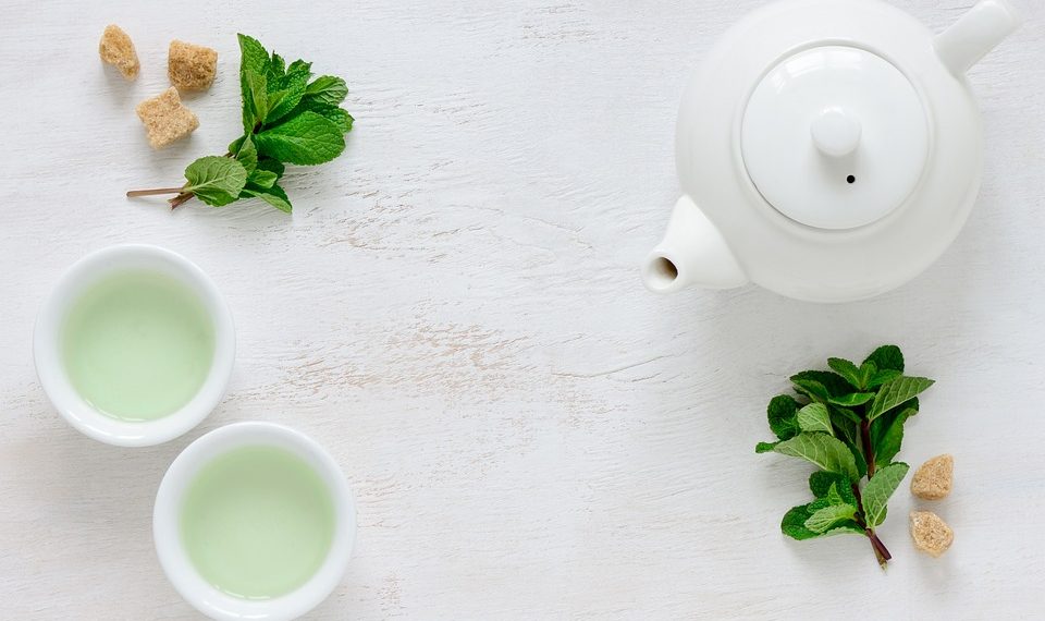 White teapot and cups with mint leaves and sugar cubes on a table.