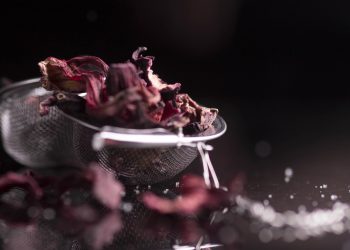 Dried hibiscus flowers in a metal strainer on a dark background.