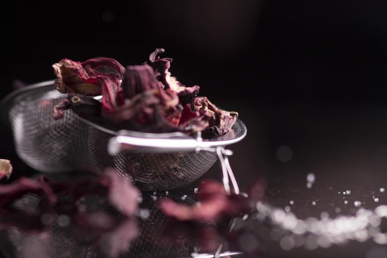 Dried hibiscus flowers in a metal strainer on a dark background.