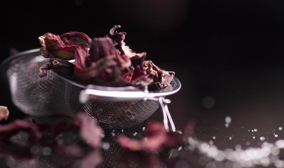 Dried hibiscus flowers in a metal strainer on a dark background.