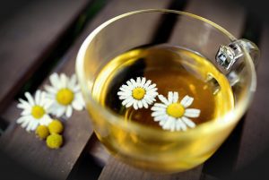 Chamomile tea in a glass cup with floating flowers.