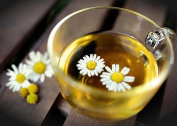 Chamomile tea in a glass cup with floating flowers.