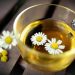 Chamomile tea in a glass cup with floating flowers.