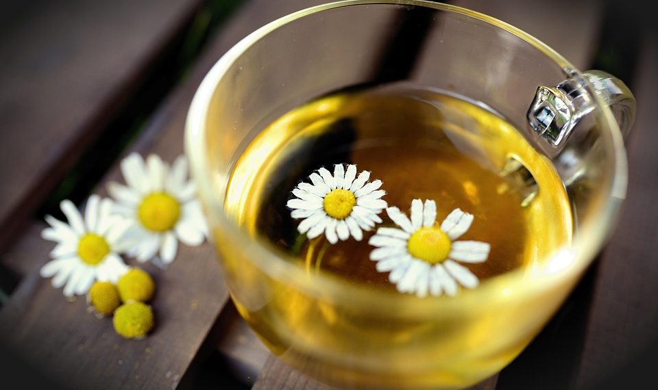 Chamomile tea in a glass cup with floating flowers.