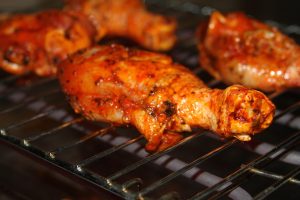 Barbecue chicken drumsticks grilling on a rack.