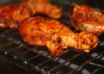 Barbecue chicken drumsticks grilling on a rack.