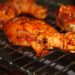 Barbecue chicken drumsticks grilling on a rack.