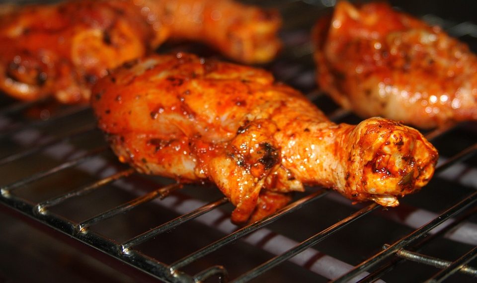 Barbecue chicken drumsticks grilling on a rack.