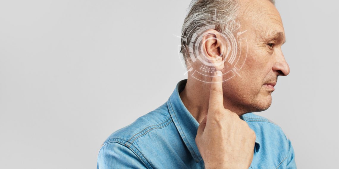 Man in denim shirt pointing at ear with digital graphics.