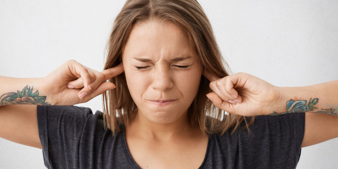 Person covering ears with fingers, eyes closed in stress.