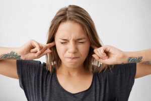 Person covering ears with fingers, eyes closed in stress.