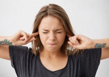 Person covering ears with fingers, eyes closed in stress.
