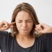 Person covering ears with fingers, eyes closed in stress.