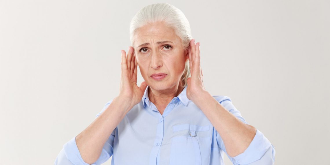 Senior woman holding her ears in discomfort.