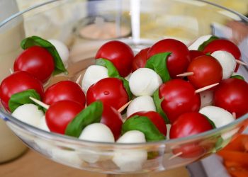Caprese skewers with tomatoes, mozzarella, and basil in a glass bowl.