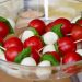 Caprese skewers with tomatoes, mozzarella, and basil in a glass bowl.