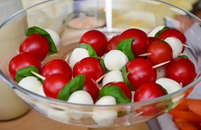 Caprese skewers with tomatoes, mozzarella, and basil in a glass bowl.