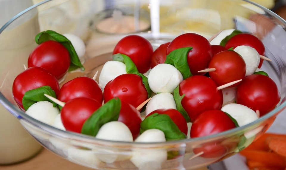 Caprese skewers with tomatoes, mozzarella, and basil in a glass bowl.