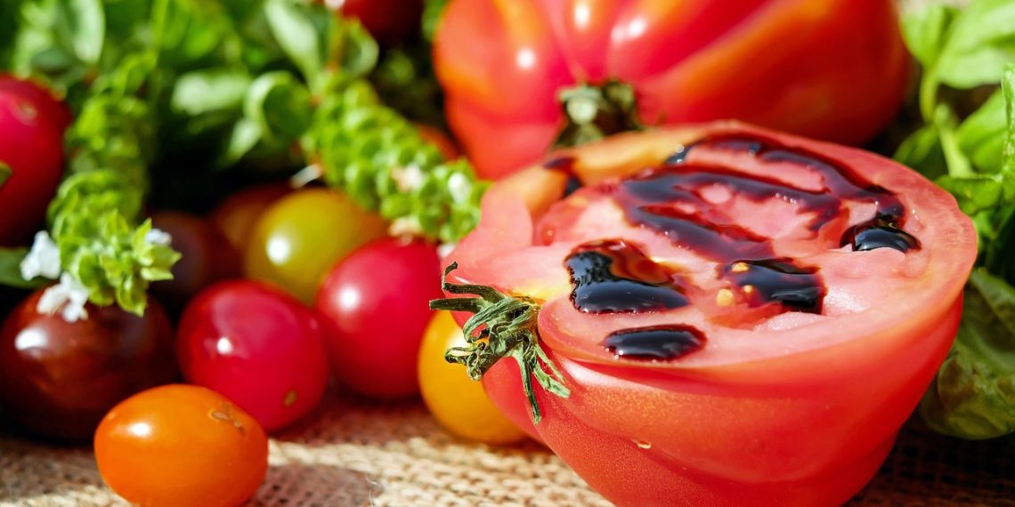 A ripe tomato, cut in half and drizzled with balsamic glaze, surrounded by colorful cherry tomatoes and fresh herbs.