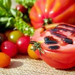A ripe tomato, cut in half and drizzled with balsamic glaze, surrounded by colorful cherry tomatoes and fresh herbs.