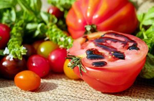 A ripe tomato, cut in half and drizzled with balsamic glaze, surrounded by colorful cherry tomatoes and fresh herbs.
