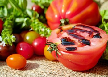 A ripe tomato, cut in half and drizzled with balsamic glaze, surrounded by colorful cherry tomatoes and fresh herbs.