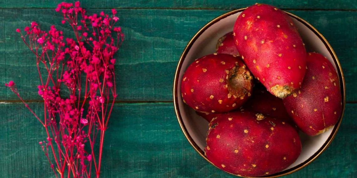 Prickly pears in a bowl with vibrant pink flowers nearby.