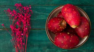 Prickly pears in a bowl with vibrant pink flowers nearby.