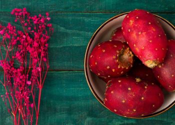 Prickly pears in a bowl with vibrant pink flowers nearby.