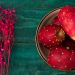 Prickly pears in a bowl with vibrant pink flowers nearby.
