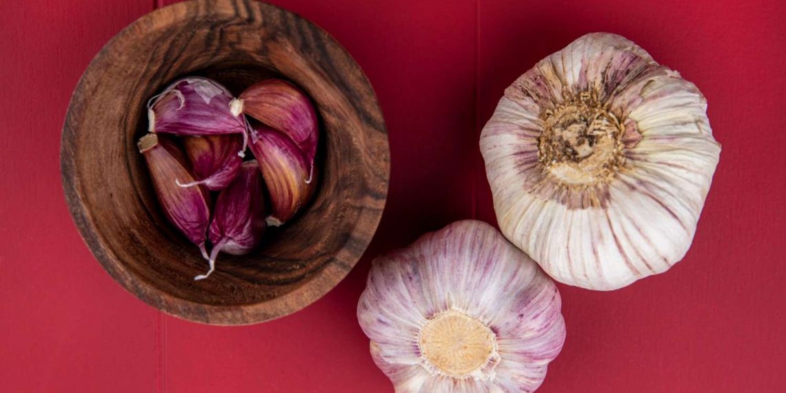 Whole and peeled garlic on red background.