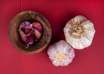 Whole and peeled garlic on red background.