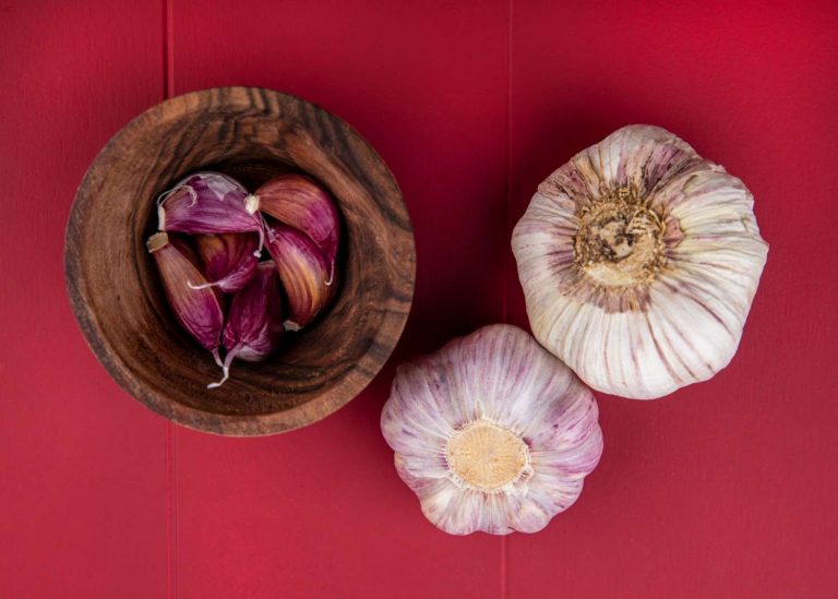 Whole and peeled garlic on red background.