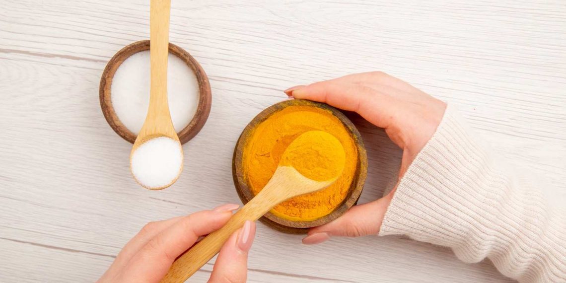 Hands holding bowls of turmeric and salt with wooden spoons.