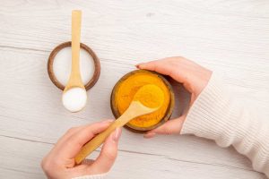 Hands holding bowls of turmeric and salt with wooden spoons.