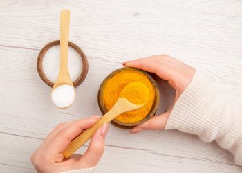 Hands holding bowls of turmeric and salt with wooden spoons.