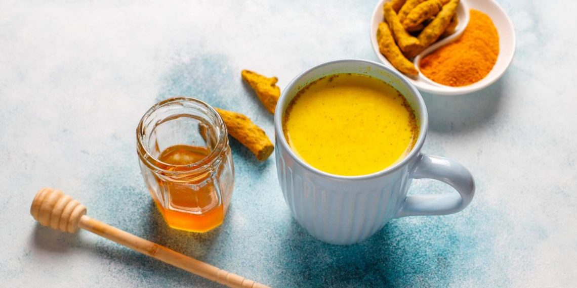 Turmeric latte with honey and fresh turmeric on a table.