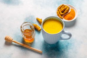 Turmeric latte with honey and fresh turmeric on a table.