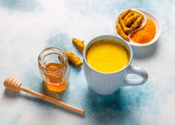 Turmeric latte with honey and fresh turmeric on a table.