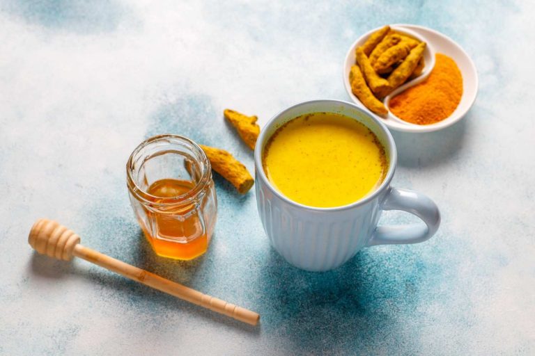 Turmeric latte with honey and fresh turmeric on a table.