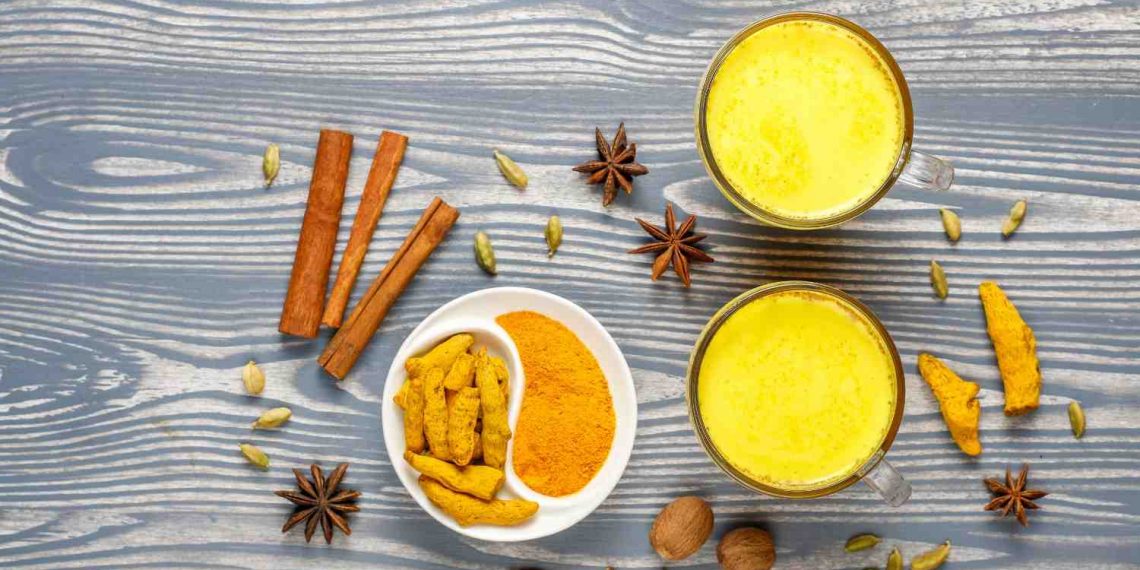 Golden turmeric milk surrounded by spices on a wooden table.