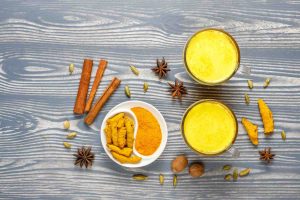 Golden turmeric milk surrounded by spices on a wooden table.