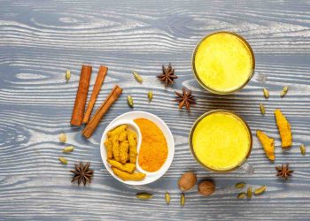 Golden turmeric milk surrounded by spices on a wooden table.