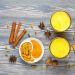 Golden turmeric milk surrounded by spices on a wooden table.